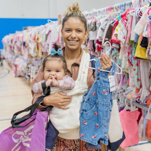 A mom and grandmother stand beside a rack of clothing at a JBF sale in Texas.